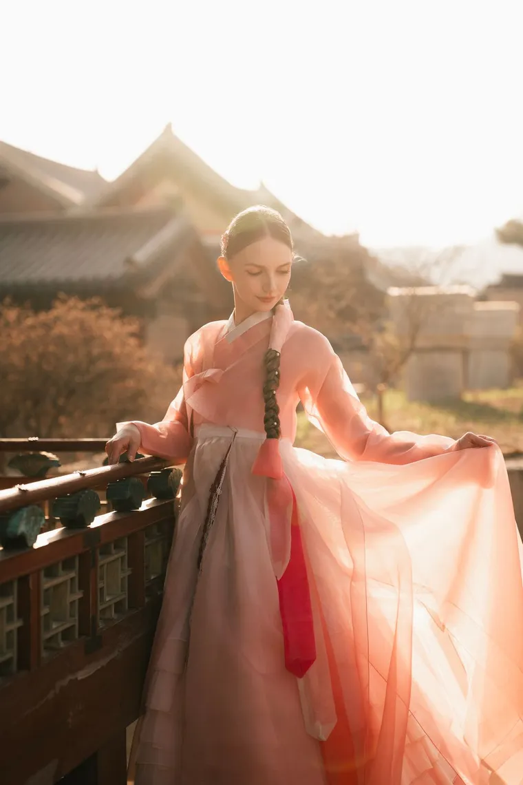 Woman in a pink hanbok holding her skirt at a palace railing