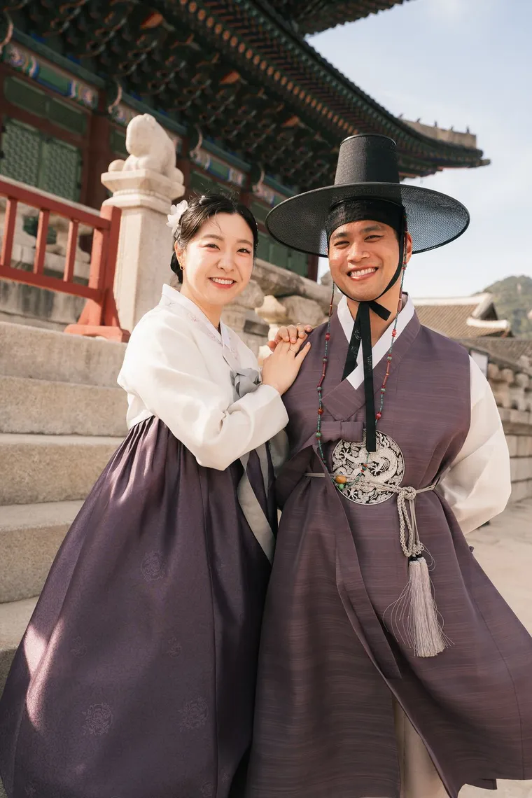 Couple in purple hanbok smiling on a palace stair