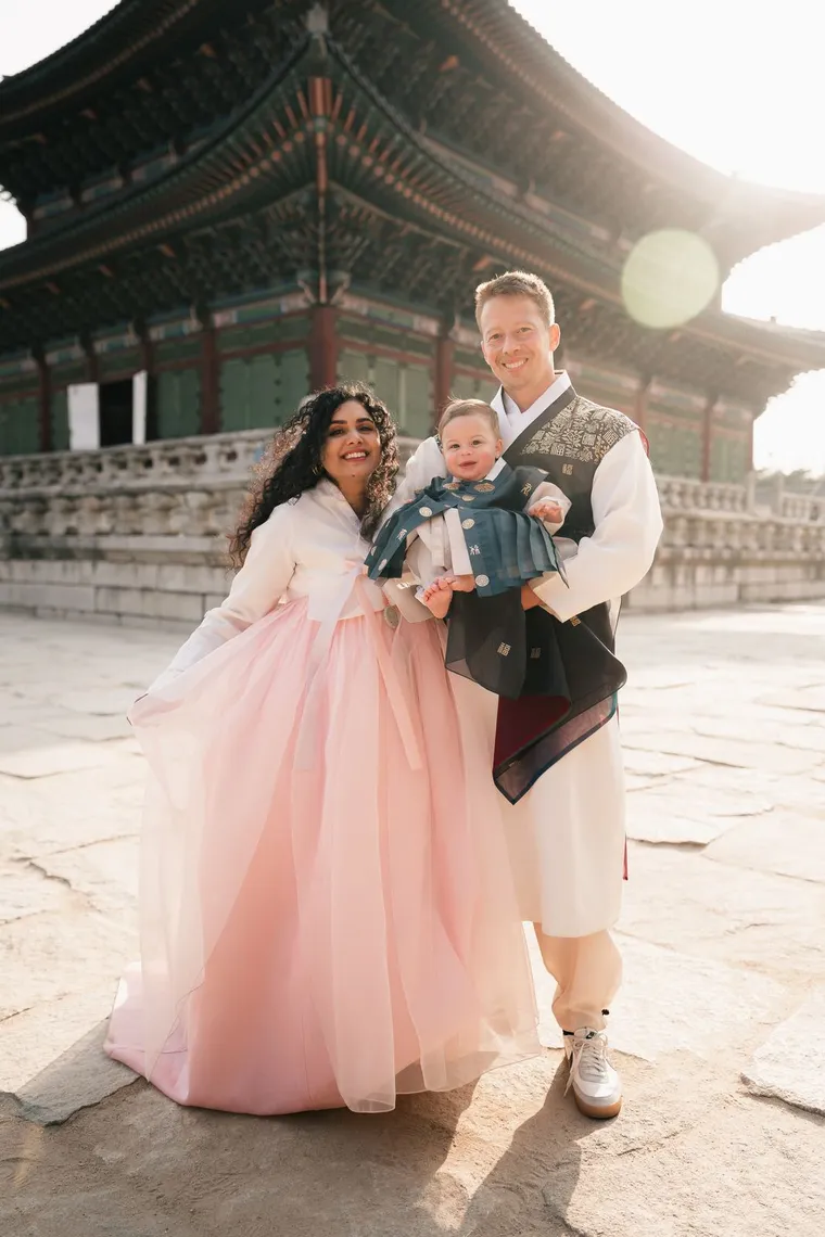 Family with a baby in hanbok standing beside a palace hall