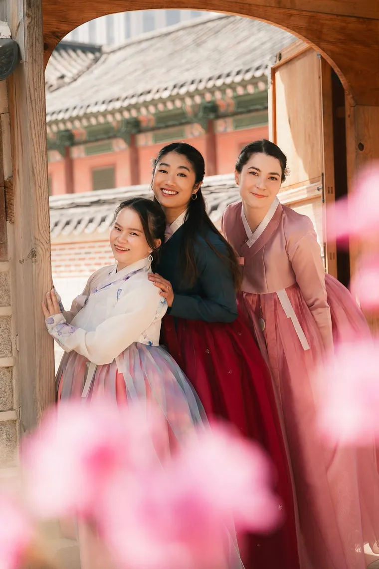 Three friends in pink and blue hanbok posing among azaleas