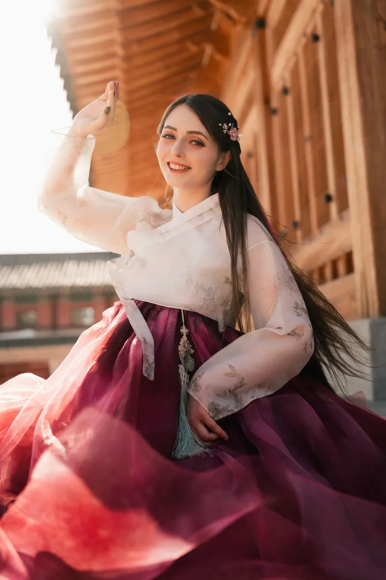 Woman in a crimson hanbok skirt smiling on a palace stair