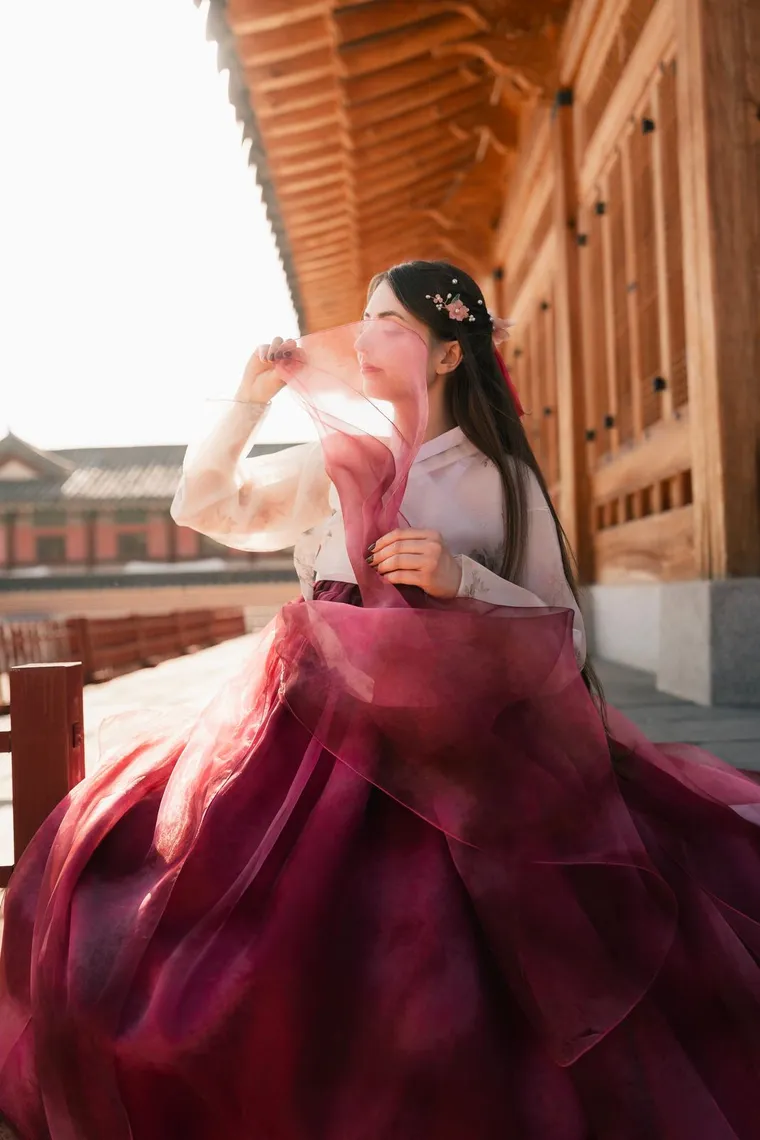 Woman in a crimson hanbok lifting the sheer sleeve of her jacket