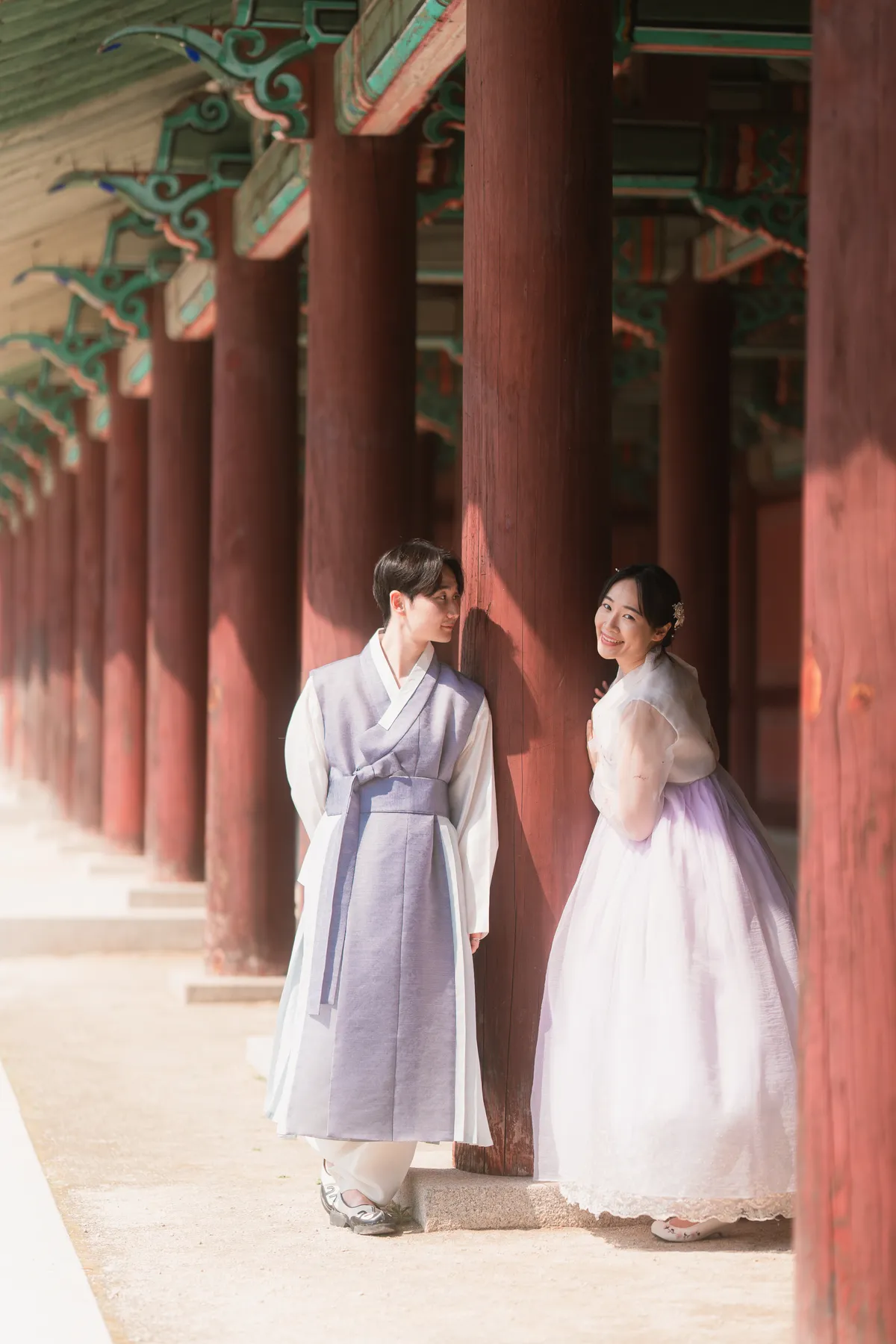 Couple in hanbok between the red columns of a palace corridor, Seoul