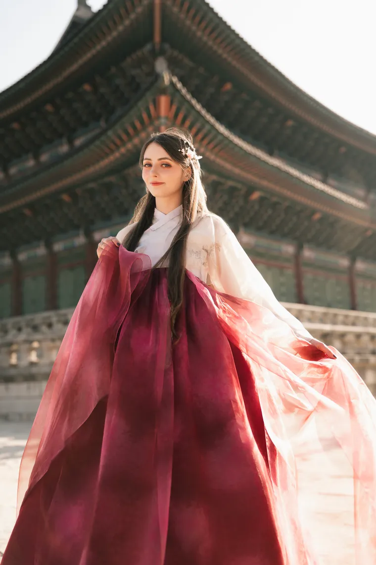 Woman in a crimson hanbok skirt beneath the painted eaves of a palace hall