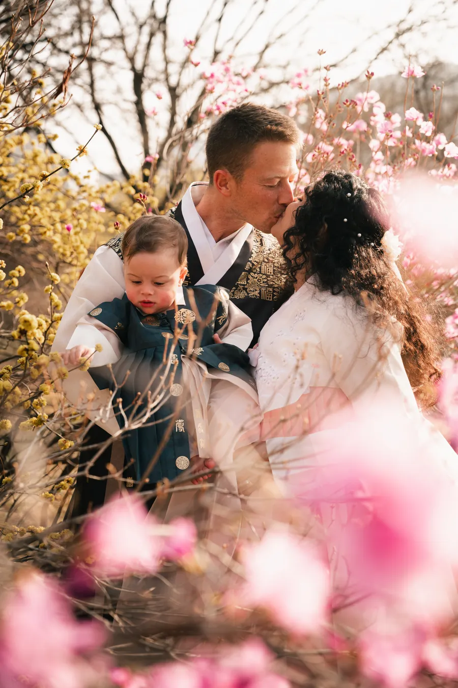 Family with a baby, all in hanbok, among spring blossoms in a Seoul palace courtyard