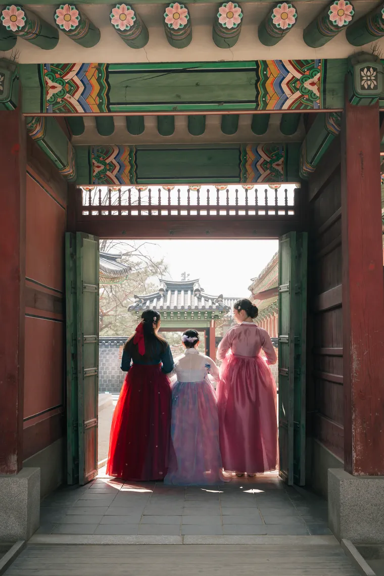 Group of friends in hanbok seen through a palace gateway, framed by the dark timber doorway