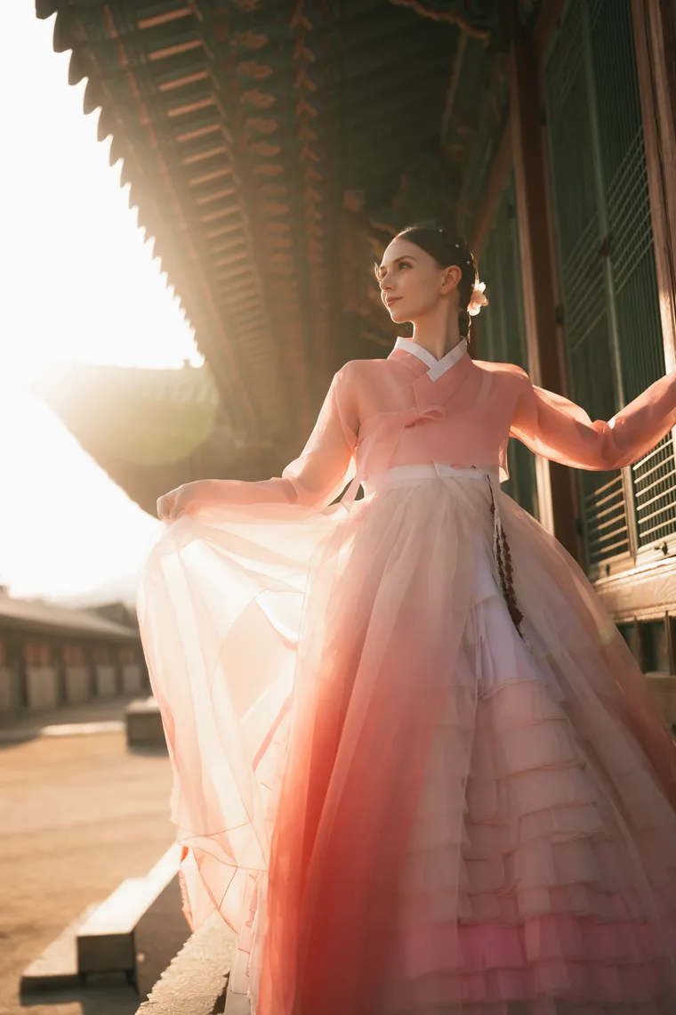 Woman in pink hanbok turning in a palace courtyard, her skirt catching the backlight